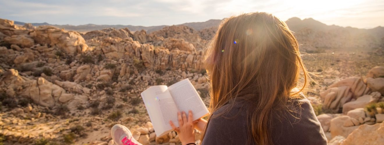 woman sitting on rock formation while reading book