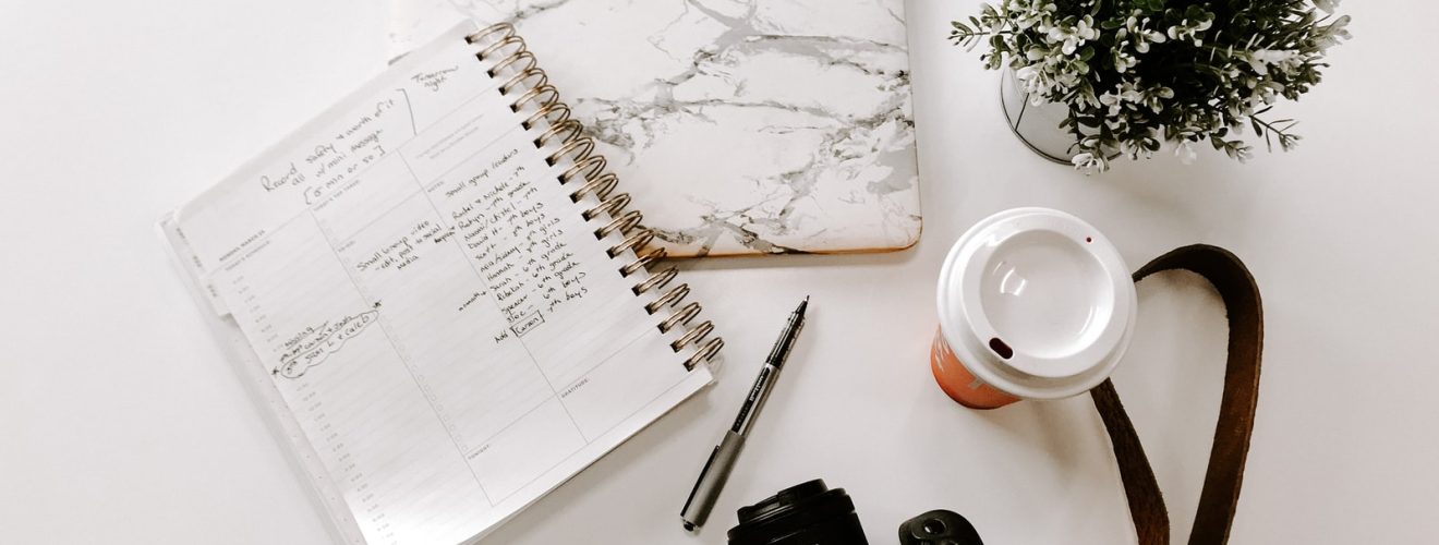 black nikon dslr camera on white notebook beside white ceramic mug