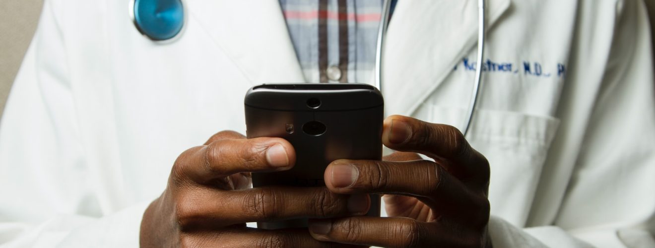 person wearing lavatory gown with green stethoscope on neck using phone while standing