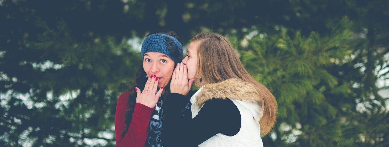 woman whispering on woman's ear while hands on lips
