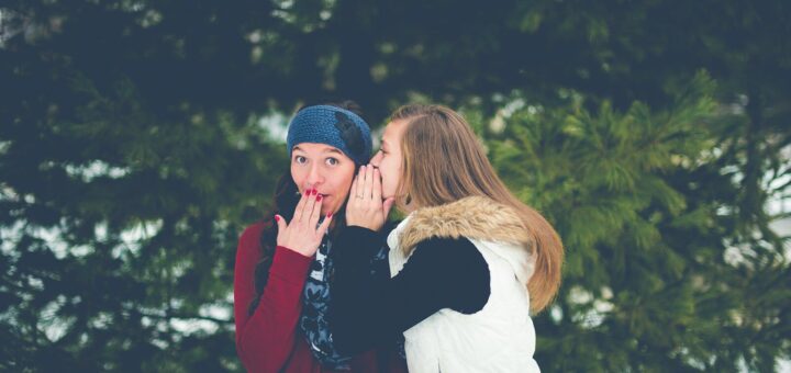 woman whispering on woman's ear while hands on lips
