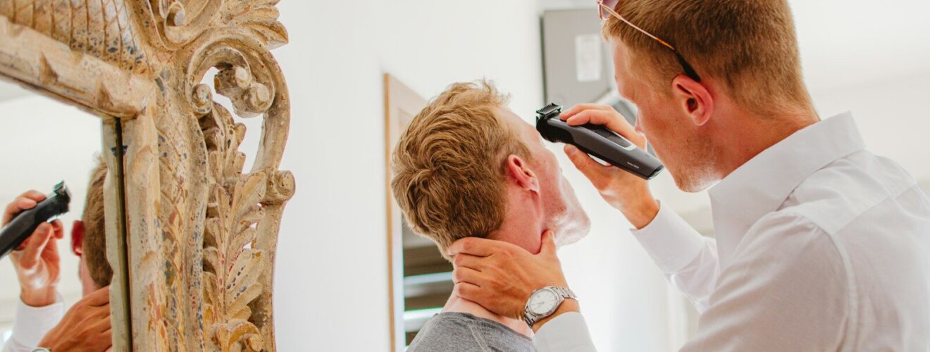 Man shaving another man's face with electric razor.