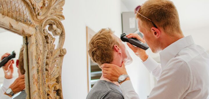 Man shaving another man's face with electric razor.
