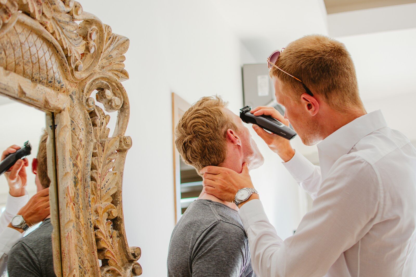 Man shaving another man's face with electric razor.